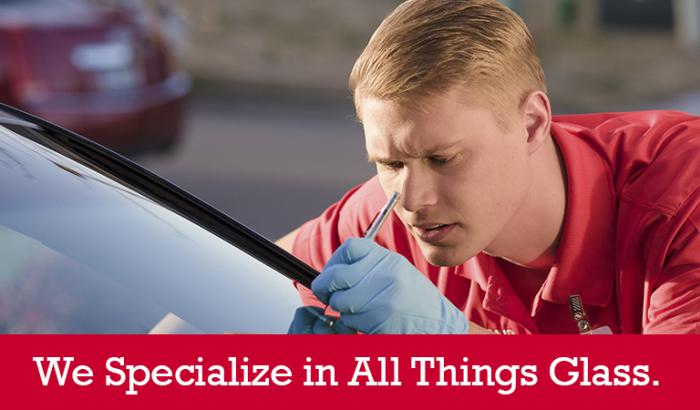 Closeup of a Glass Doctor specialist repairing a crack in a windshield with &quot;We Specialize in All Things Glass&quot; written below it
