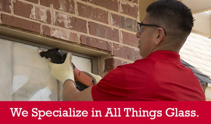 Glass Doctor specialist repairing a home window seal with &quot;We Specialize in All Things Glass&quot; written below it